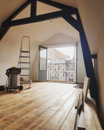 Lichte, ruime studio met houten vloer en strak afgewerkte wanden. De muren zijn pas gewit. 